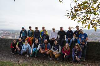 Gruppe junger Menschen sitzt und kniet auf einer Mauer vor einer Stadt