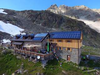 Berghütte mit Solaranlage auf dem Dach, im Hintergrund Berglandschaft
