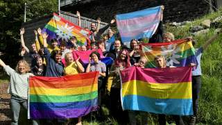 Gruppe von Menschen mit Pride-, Bi-Pride- und Trans-Pride-Flaggen strecken Hände in die Luft