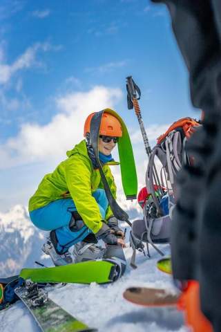 Eine Frau sitzt mit viel Ski- und Bergequipment im Schnee
