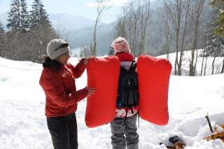 Zwei Menschen stehen im Schnee; die rechte Person trägt einen Airbag-Rucksack