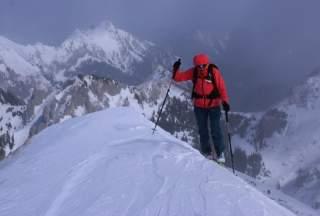 Ein Wanderer in einer roten Jacke steht an einem Schneebedeckten Bergkamm