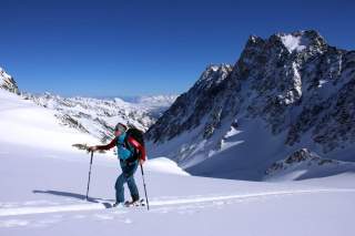 Ein Skibergsteiger in hellblauer Jacke besteigt bei bestem Wetter einen Berg.