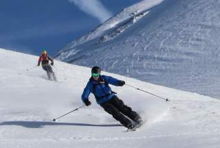 Zwei Skifahrer fahren bei blauem Himmel einen Hang runter