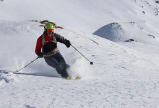 Eine Person in Skiausrüstung fährt an einem klaren Tag einen verschneiten Berghang hinunter.
