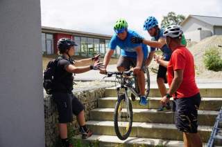 Einem Jungen wird dabei geholfen mit dem Mountainbike eine Treppe runterzufahren