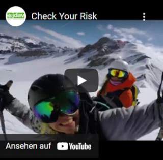 Zwei Personen in Ski- oder Snowboardausrüstung posieren lachend vor einer verschneiten Berglandschaft. Beide tragen Helme und Skibrillen, und der Himmel ist teilweise bewölkt.