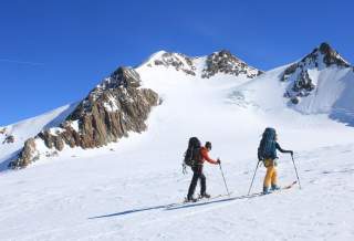 Zwei Skibergsteiger sind bei blauen Himmel an einem Hang unterwegs
