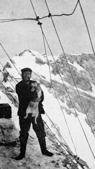 Ein Mann mit seinem Hund auf dem Arm stehen auf einem schneebedeckten Gipfel