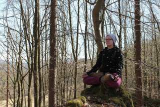 Eine Frau sitz im Yoga-Sitz in einem kahlen Wald