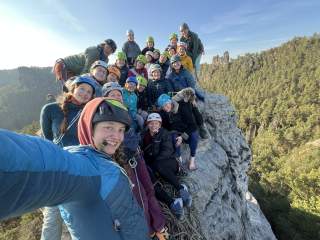 Eine Gruppe junger Frauen steht auf einem Berggipfel und blickt gemeinsam in die umliegende Berglandschaft