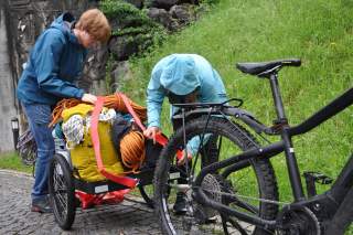 Zwei Menschen packen einen Fahrradanhänger mit Klettermaterialien.