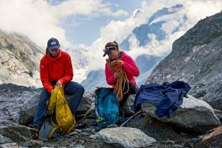 Zwei Wander*innen sitzen auf Felsen und packen ihre Rucksäcke