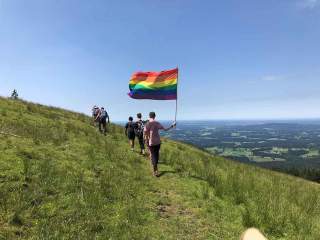 Eine Person läuft mit Regenbogenflagge über einen Berghang